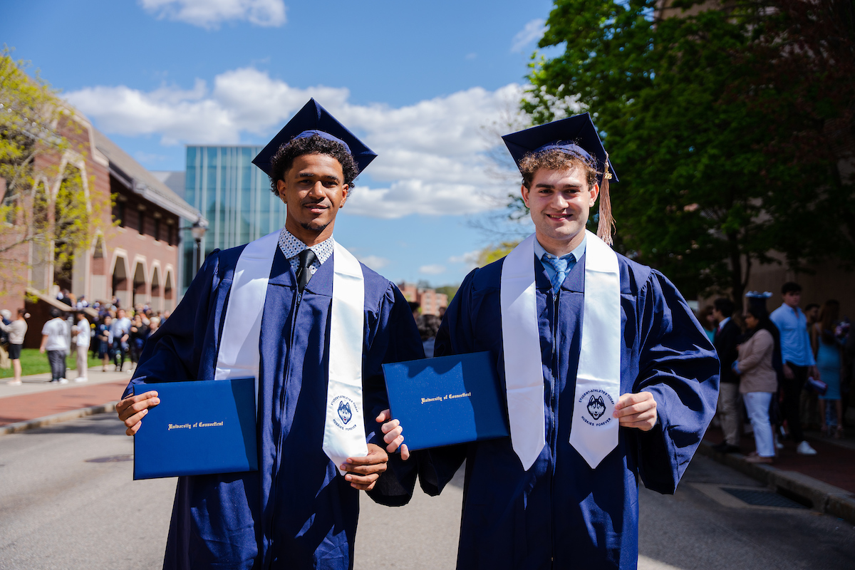 Two male student athletes pose with their diplomas at Commencement